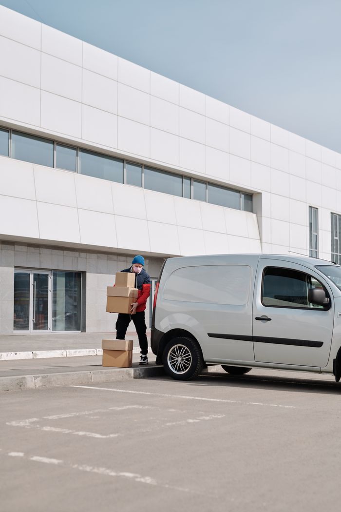 services-06 Delivery worker in mask and male-loading packages into a white van outdoors.