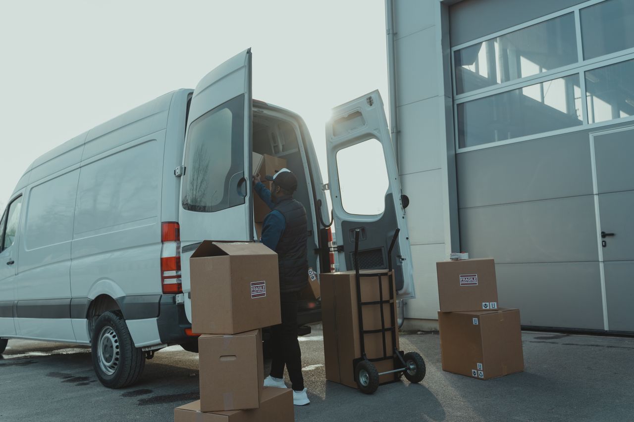 home-hero Courier loading cardboard boxes into a delivery van outside a warehouse.